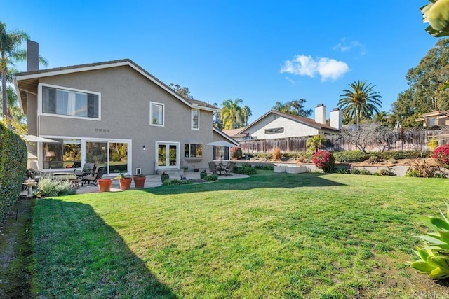 rear view of property with a lawn, fence, and stucco siding