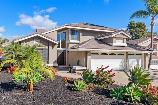 traditional home with a garage, driveway, a tile roof, and stucco siding