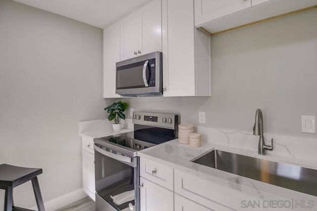 kitchen featuring light hardwood / wood-style floors, light stone countertops, appliances with stainless steel finishes, white cabinetry, and sink