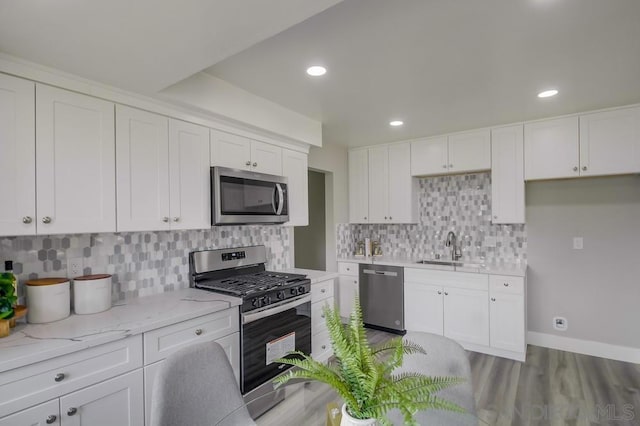 kitchen with hardwood / wood-style floors, light stone countertops, white cabinets, sink, and stainless steel appliances