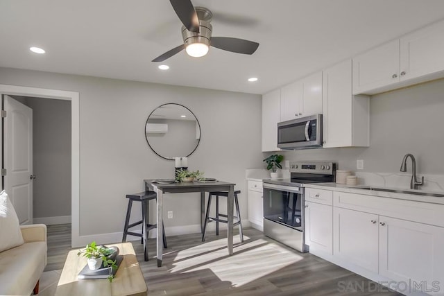 kitchen with hardwood / wood-style floors, appliances with stainless steel finishes, white cabinetry, sink, and ceiling fan