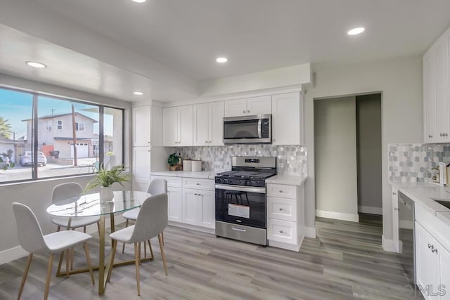 kitchen featuring backsplash, white cabinets, light wood-type flooring, and appliances with stainless steel finishes