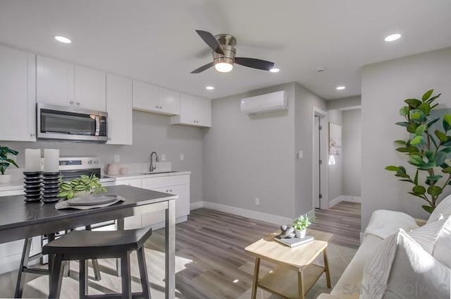 kitchen with appliances with stainless steel finishes, a wall mounted air conditioner, white cabinetry, sink, and light wood-type flooring