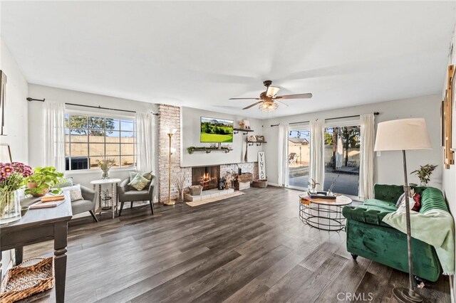 living room with ceiling fan, a wealth of natural light, dark wood-type flooring, and a fireplace