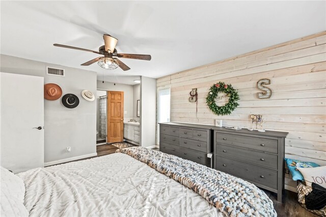 bedroom featuring ceiling fan, wood walls, dark hardwood / wood-style floors, and ensuite bath