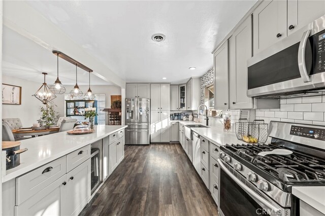 kitchen featuring hanging light fixtures, dark hardwood / wood-style flooring, sink, appliances with stainless steel finishes, and decorative backsplash