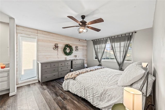 bedroom featuring ceiling fan, access to exterior, dark hardwood / wood-style floors, and wooden walls