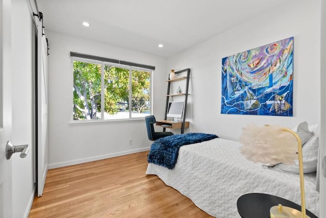 bedroom with wood-type flooring and a barn door