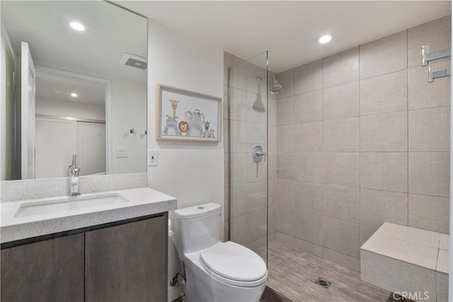 bathroom with toilet, vanity, and a tile shower