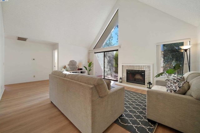 living room featuring high vaulted ceiling, light hardwood / wood-style flooring, and a tile fireplace