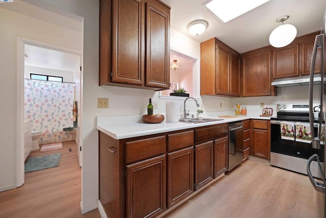 kitchen with stainless steel appliances, hanging light fixtures, sink, and light hardwood / wood-style flooring