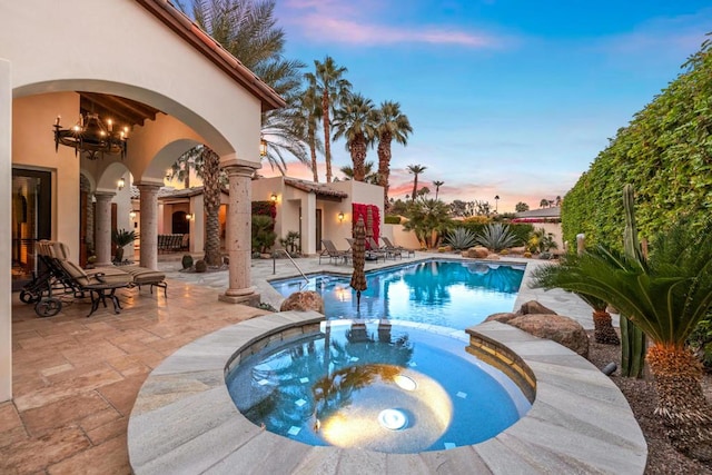 pool at dusk with an in ground hot tub and a patio area