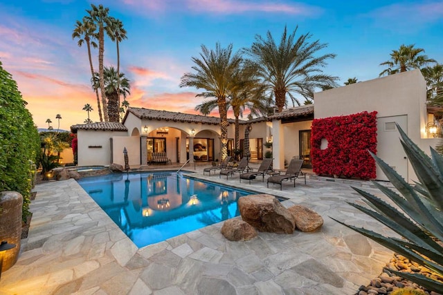 pool at dusk with an in ground hot tub and a patio