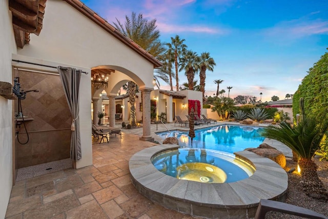 pool at dusk featuring an in ground hot tub and a patio