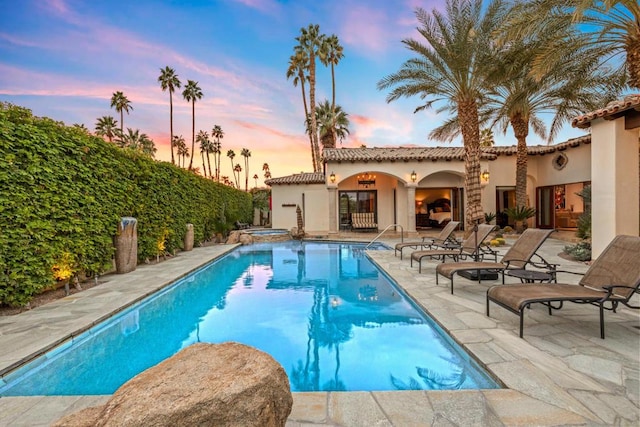 pool at dusk with an in ground hot tub and a patio area