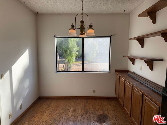 unfurnished dining area with a textured ceiling, dark hardwood / wood-style floors, and a notable chandelier