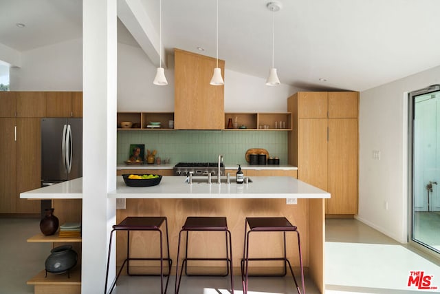 kitchen featuring tasteful backsplash, a breakfast bar area, stainless steel fridge, and hanging light fixtures