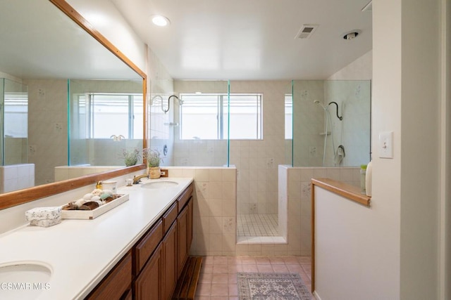 bathroom with tile patterned flooring, vanity, a wealth of natural light, and a tile shower