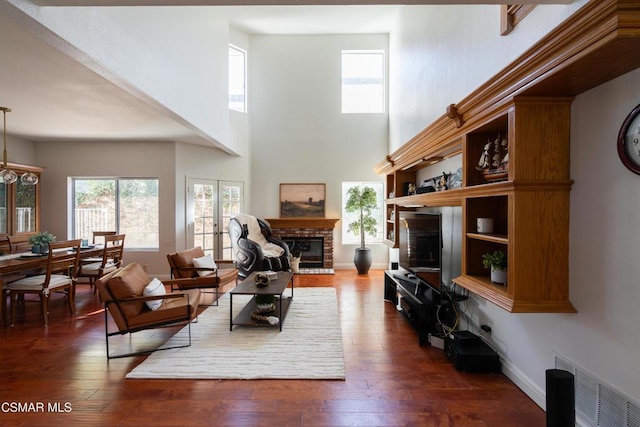 living room with a high ceiling, a brick fireplace, dark hardwood / wood-style flooring, and french doors