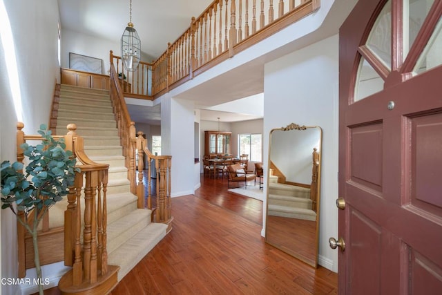 foyer entrance featuring a towering ceiling, hardwood / wood-style floors, and a notable chandelier