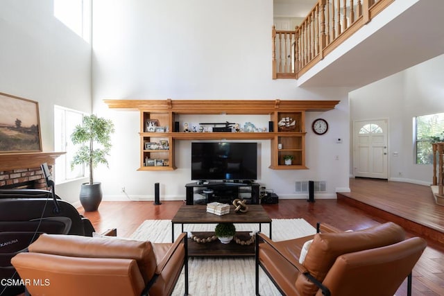 living room featuring a towering ceiling, hardwood / wood-style floors, and a brick fireplace