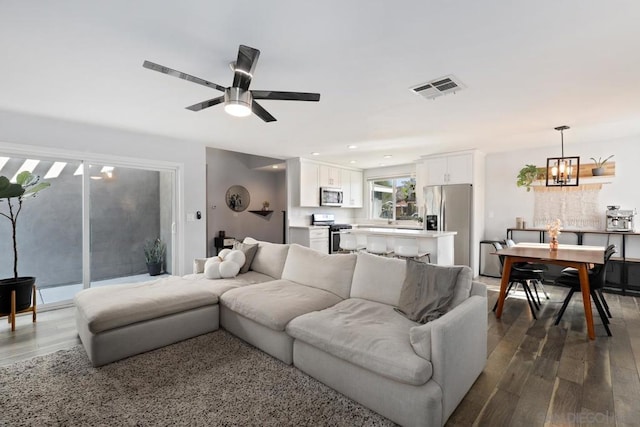 living room featuring ceiling fan with notable chandelier and dark hardwood / wood-style floors