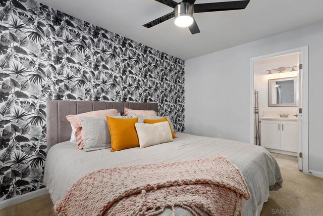 bedroom with sink, ceiling fan, light colored carpet, and ensuite bath