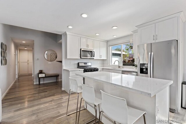 kitchen featuring light hardwood / wood-style flooring, white cabinets, a kitchen bar, a center island, and stainless steel appliances