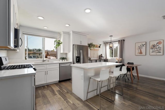 kitchen with pendant lighting, dark wood-type flooring, white cabinetry, a kitchen island, and stainless steel appliances