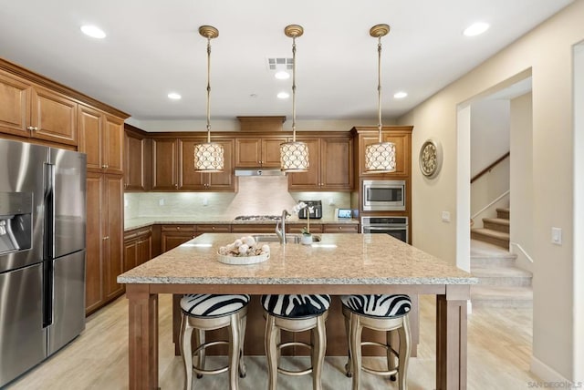 kitchen featuring light stone countertops, appliances with stainless steel finishes, decorative backsplash, pendant lighting, and an island with sink