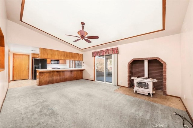 unfurnished living room featuring ceiling fan, a wood stove, light colored carpet, and lofted ceiling