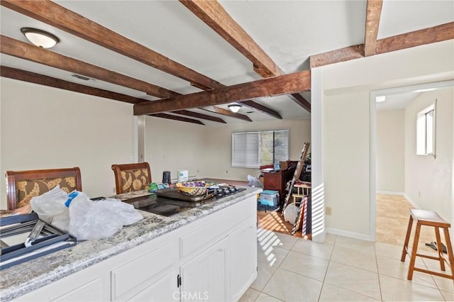 kitchen featuring white cabinetry, light tile patterned floors, light stone counters, and beamed ceiling