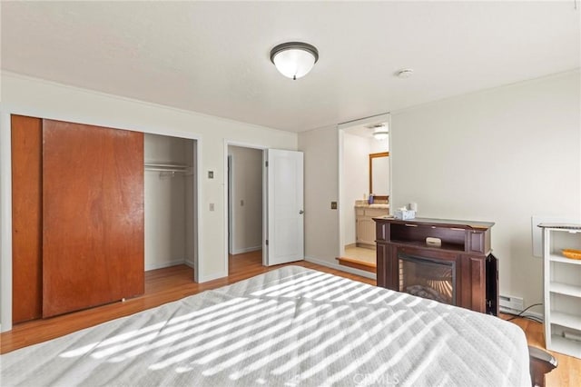 bedroom featuring a baseboard radiator, light hardwood / wood-style floors, ensuite bath, and a closet