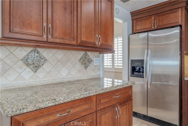 kitchen featuring stainless steel refrigerator with ice dispenser, decorative backsplash, and light stone countertops