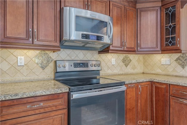 kitchen with decorative backsplash, light stone counters, and stainless steel appliances