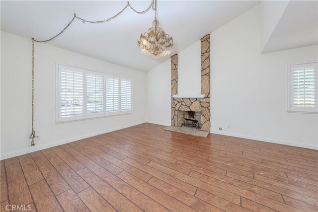 unfurnished living room with light wood-type flooring, an inviting chandelier, a fireplace, and lofted ceiling