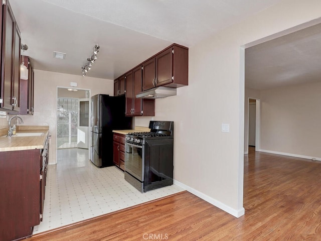 kitchen with sink, black gas stove, light hardwood / wood-style floors, and stainless steel fridge