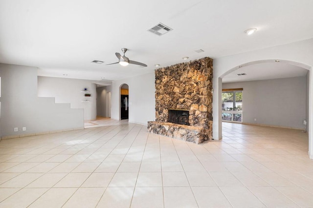 unfurnished living room featuring ceiling fan, light tile patterned flooring, and a stone fireplace