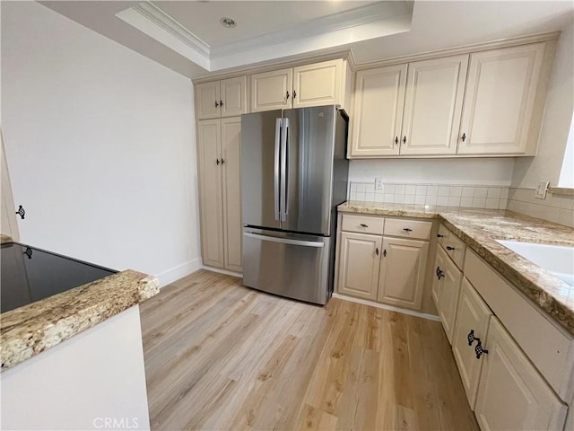 kitchen featuring cream cabinets, a tray ceiling, ornamental molding, light hardwood / wood-style floors, and stainless steel refrigerator