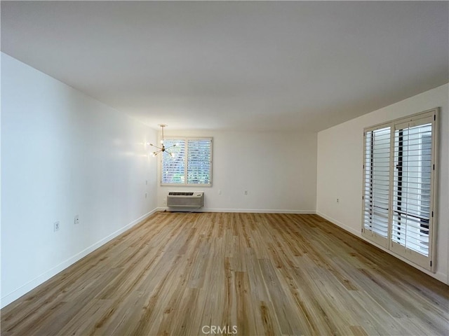 unfurnished living room featuring an AC wall unit, an inviting chandelier, and light wood-type flooring