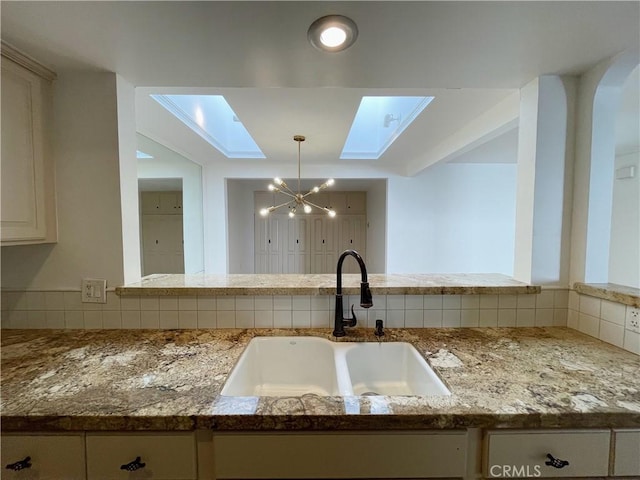 kitchen featuring pendant lighting, sink, tasteful backsplash, light stone countertops, and a skylight