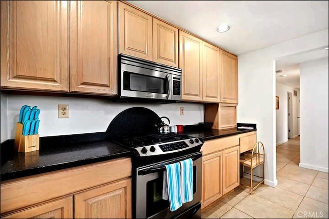 kitchen featuring light tile patterned flooring, light brown cabinets, baseboards, appliances with stainless steel finishes, and dark stone countertops