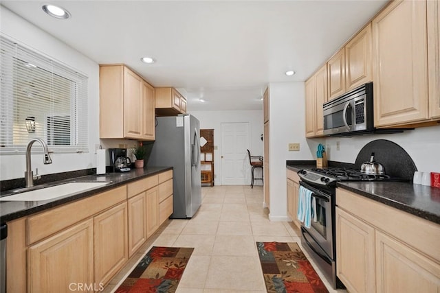 kitchen with sink, appliances with stainless steel finishes, dark stone countertops, light tile patterned flooring, and light brown cabinetry