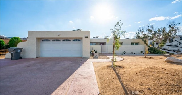 adobe home with driveway, an attached garage, fence, and stucco siding