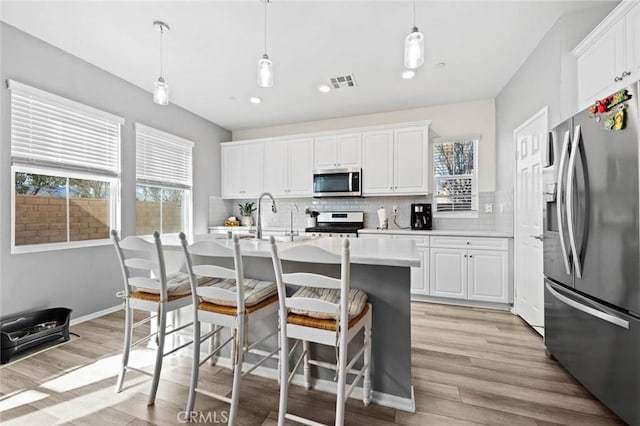 kitchen featuring white cabinets, a kitchen island with sink, hanging light fixtures, and stainless steel appliances