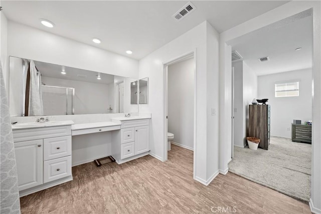 bathroom featuring wood-type flooring, toilet, a shower with shower door, and vanity