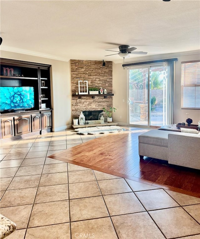 unfurnished living room with ceiling fan, tile patterned floors, ornamental molding, and a stone fireplace