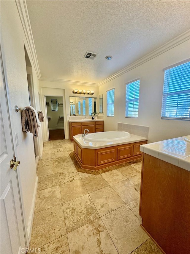 bathroom with a textured ceiling, a bathing tub, vanity, and crown molding