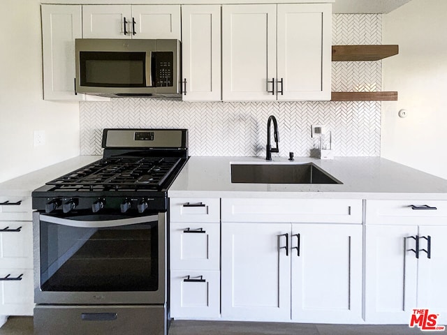 kitchen featuring appliances with stainless steel finishes, white cabinetry, sink, backsplash, and light stone counters