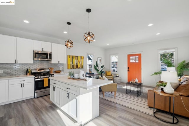 kitchen with tasteful backsplash, hanging light fixtures, a kitchen island, stainless steel appliances, and white cabinets